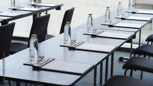 Plastic water bottles, Drinking glasses with pencil and white papers setup on the table prepared for seminar or business meeting in the hotel conference room