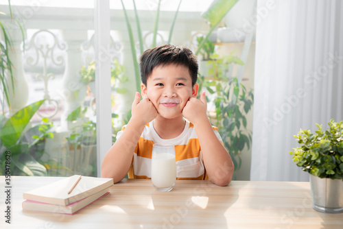 Adorable happy young Asian boy having breakfast and drinking milk at home in the morning; looking at camera