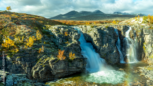 The bridal veil waterfall in Rondane national park in Norway during autumn. Colorful scenery and snow capped mountains in the background.