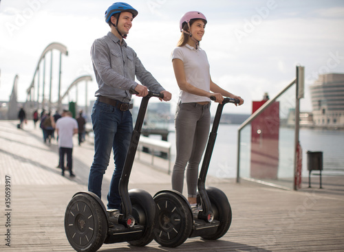 young couple guy and girl are walking on the segway along the board paved promenade in the port of a European city