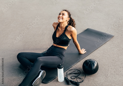 Happy woman sitting on a mat and looking up after evening work out