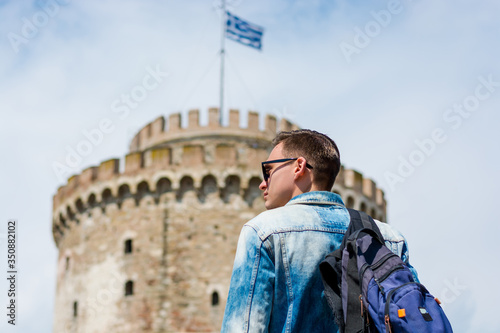 Young handsome man in sunglasses, tourist, with backpack is watching on a White Tower in the Thessaloniki, Greece