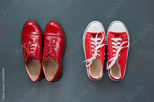 Fashion and style. Classic women's red patent leather shoes and trendy youth red sneakers on grey wooden background. Top view.