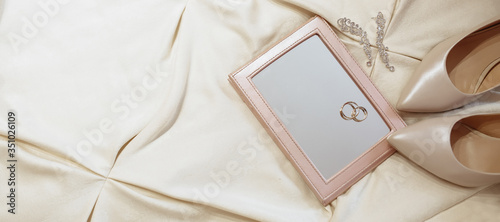 Two gold rings lie on the mirror, earrings and shoes of the bride lie on the bed. Wedding morning, girl preparation. Details of the day's wedding in pastel colors.