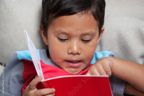 A preschooler pronouncing simple phonics is reading from an early reader style story book.