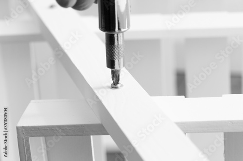 Man assembling a white flat pack ladder shelving unit with a screwdriver. Flat pack assembly concept