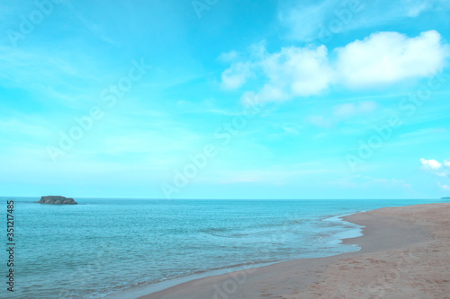 Beautiful calm ocean waves reaching tropical sandy beach on sunny blue sky background with puffy fluffy clouds & white cloudscape in morning sunlight & sun rays at daylight sunshine day, free space 