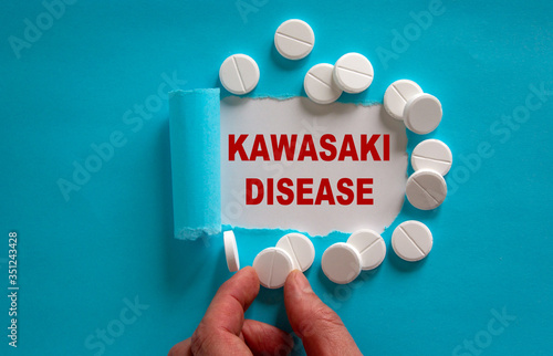 The text 'kawasaki disease' appearing behind torn blue paper. White pills and male hand. Beautiful blue and white background.