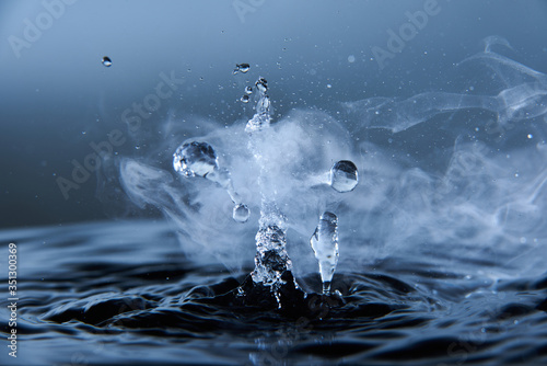Boiling water splash with steam on dark blue background closeup