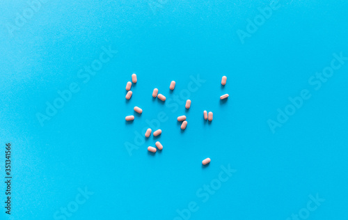 Pink pills on blue background. Medicine, medication, painkillers, tablet, medicaments, drugs, antibiotic, vitamin, treatment. Pharmacy theme. Top view on the pills scattered on the blue surface.