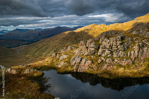 Little pond and dramatic rocky terrain features near Beinn a'Chroin, mountain in Scottish Highlands, with glen Falloch in the distance. Beautiful Scottish Higlands landscape.