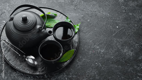 Teapot and two cups of tea on a black stone background. Top view. free space for your text.