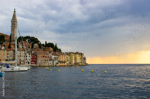 View of the typical croatian houses in the coastline of the old town of Rovinj, Croatia, with some boats on the left and the tower of the Church of St Euphemia on the top