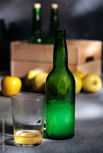 Asturian cider bottles green apples at wicker basket over wooden background