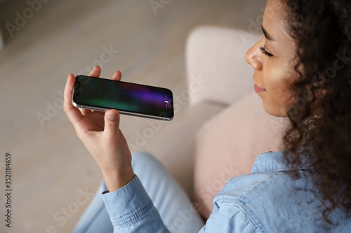 Young african woman user holding mobile phone in hand speak on speakerphone using virtual digital voice recognition assistant search on smartphone record audio message, mobile app ai tech assistance.