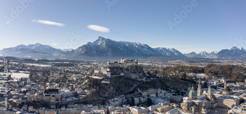 Panoramic aerial drone view of snowy Hohensalzburg fortress with view of Unesberg mountain in winter morning