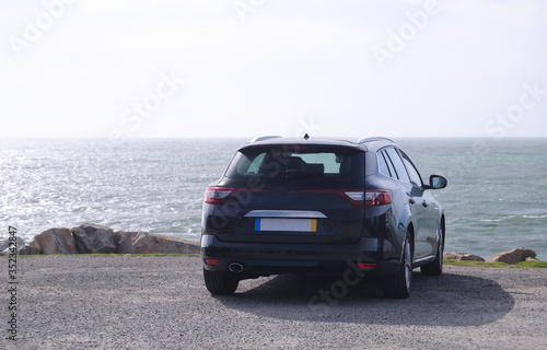 Carro preto estacionado em frente de uma falésia á beira mar virado para o horizonte