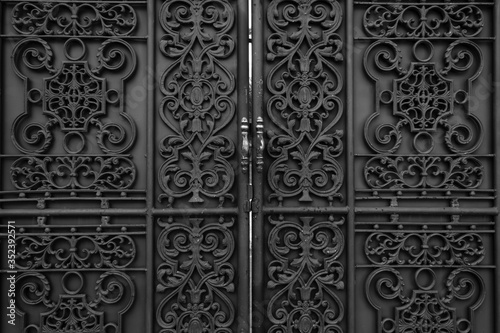 Black iron forged gate in front of the house. Classic ornamental forged metal double gates.