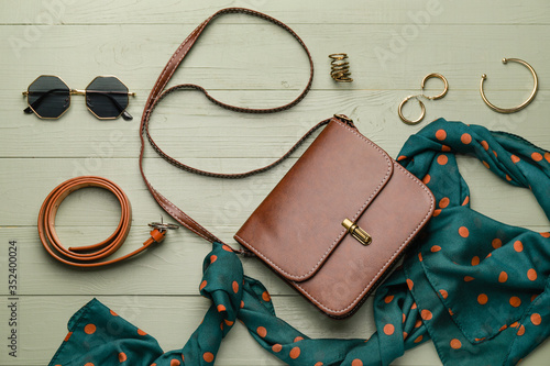 Stylish bag with female accessories on color wooden background