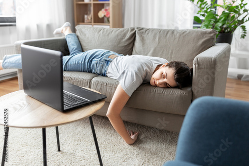 people, boredom and depression concept - bored or lazy young woman with laptop computer lying on sofa at home