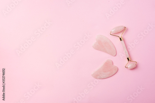 Pink gua sha facial massage roller. Anti age, lifting, toning face treatment at home. Skin care concept. Rose quartz stone roller on pink background. Copy space.