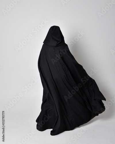 fantasy portrait of a woman wearing long black cloak. Full length standing pose with back to the camera, isolated against a studio background.