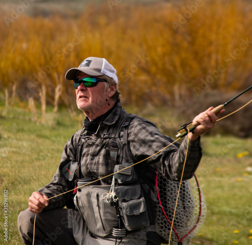 A man on the bank of a river fly fishing.