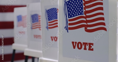 CU straight on row of voting booths at polling station during American election. US flag in background.