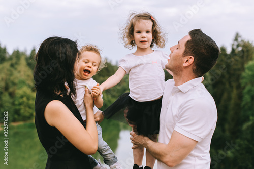 Handsome young father and beautiful mother in sunny summer nature playing with their cute small childrens