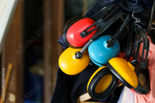 Red yellow and blue ear muffs hanging in storage basement or room in day close up ear sound noise protection