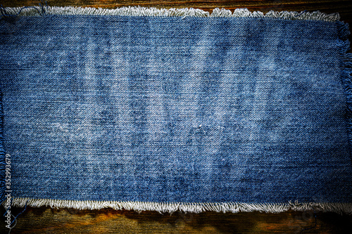 Denim blue cloth frame patch on wooden table. Denim jeans frame background. Ripped denim fabric, text place, copy space. Washed torn denim cloth with fringe edge. Fashion backdrop.