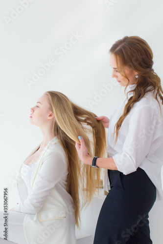 Stock Photo - Hairdresser smooths the hair of a client with a curling iron. Beautiful blonde girl in a beauty salon