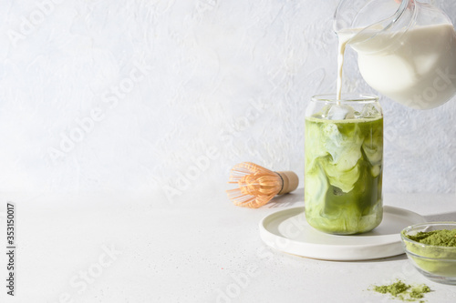 Iced Green matcha latte tea and pouring milk in glass on white background.Close up. Horizontal orientation.