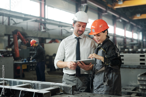 Asian metalworking specialist discussing technical sketch with engineer while they using engineering app on tablet