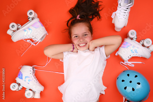 Little child with roller skates, a blue helmet on a red background, a happy smile and positive emotions. A girl of 7 years old poses and prepares for active leisure on retro ice skates.