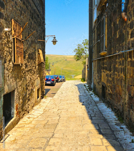  narrow street between old buildnigs and beautiful view on green hills around small town Venosa in Basilicata, South Italy 