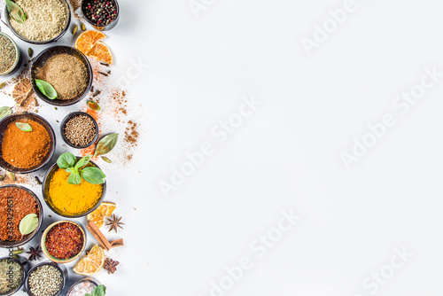 Set of Spices and herbs for cooking. Small bowls with colorful seasonings and spices - basil, pepper, saffron, salt, paprika, turmeric. On white stone table background top view copy space