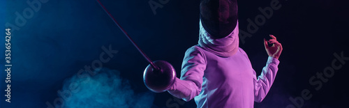 Panoramic crop of swordswoman fencing on black background with smoke and lighting