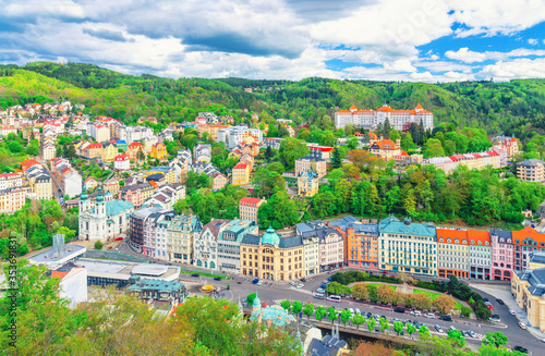 Karlovy Vary (Carlsbad) historical city centre top aerial view with colorful beautiful buildings, Slavkov Forest hills with green trees, blue sky white clouds background, West Bohemia, Czech Republic