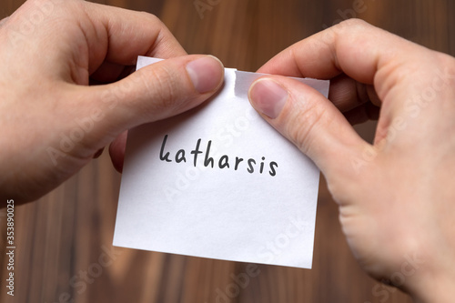 Hands of a man tearing a piece of paper with inscription katharsis