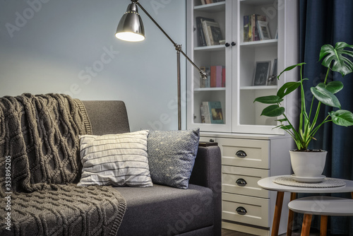 Grey couch with cushions, knitted plaid and floor lamp