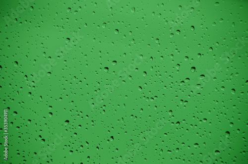 Krople wody na szybie okiennej z zielonym tłem w deszczowy dzień 