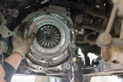 Car repair in a car service. Replacing the clutch disc of a gearbox on a car at a service station. Hands of a professional car mechanic. Cars repair technology. Technical photography.