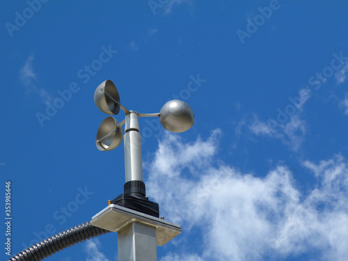 anemometer wind speed indicator measuring device fixed to aluminum bracket on tube post. meteorological device. abstract low angle view. spoon shaped semi sphere blades. clear blue sky. white clouds