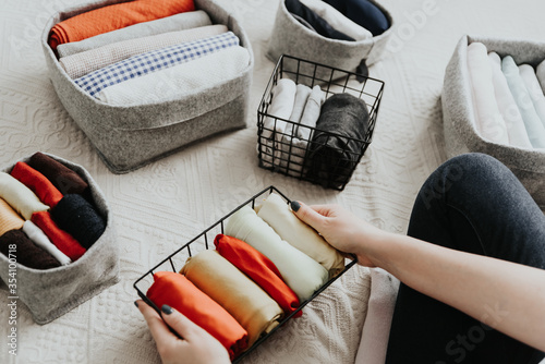 Woman organizing clothes in wardrobe, putting laundry in boxes and baskets. Concept of minimalism lifestyle and japanese t-shirt folding system. Tidy up wardrobe