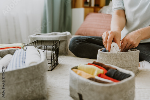 Woman folding clothes, organizing laundry in boxes and baskets. Concept of minimalist lifestyle and japanese t-shirt folding system. Minimalist wardrobe