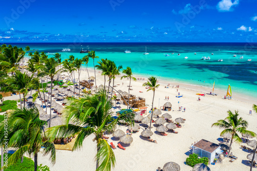 Aerial drone view of beautiful atlantic tropical beach with palms, straw umbrellas and boats. Bavaro, Punta Cana, Dominican Republic. Vacation background.