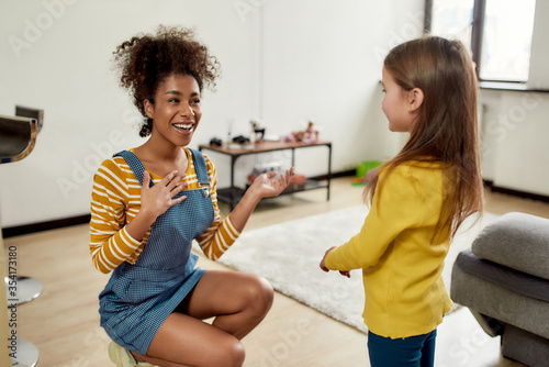 Glad to meet you. African american woman baby sitter get acquainted with caucasian cute little girl. They are smiling and talking