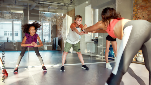 Everyday job. Portrait of teens, boys and girls warming up, exercising with female trainer in gym. Sport, healthy lifestyle, physical education concept