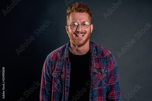 Take this ugly thing away from me. Displeased intense redhead mature guy in glasses and checkered shirt, turning away and protecting face with raised hands, seeing something disgusting over grey wall